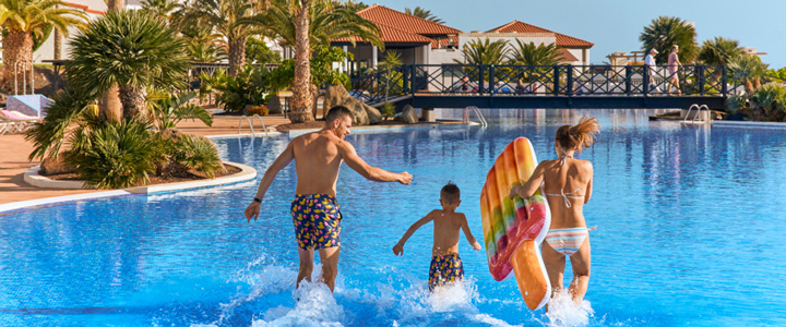 Junge Familie genießt die großzügige Poollandschaft vom Hotel Playa de Esquinzo und rennt mit Luftmatratze ins Wasser.